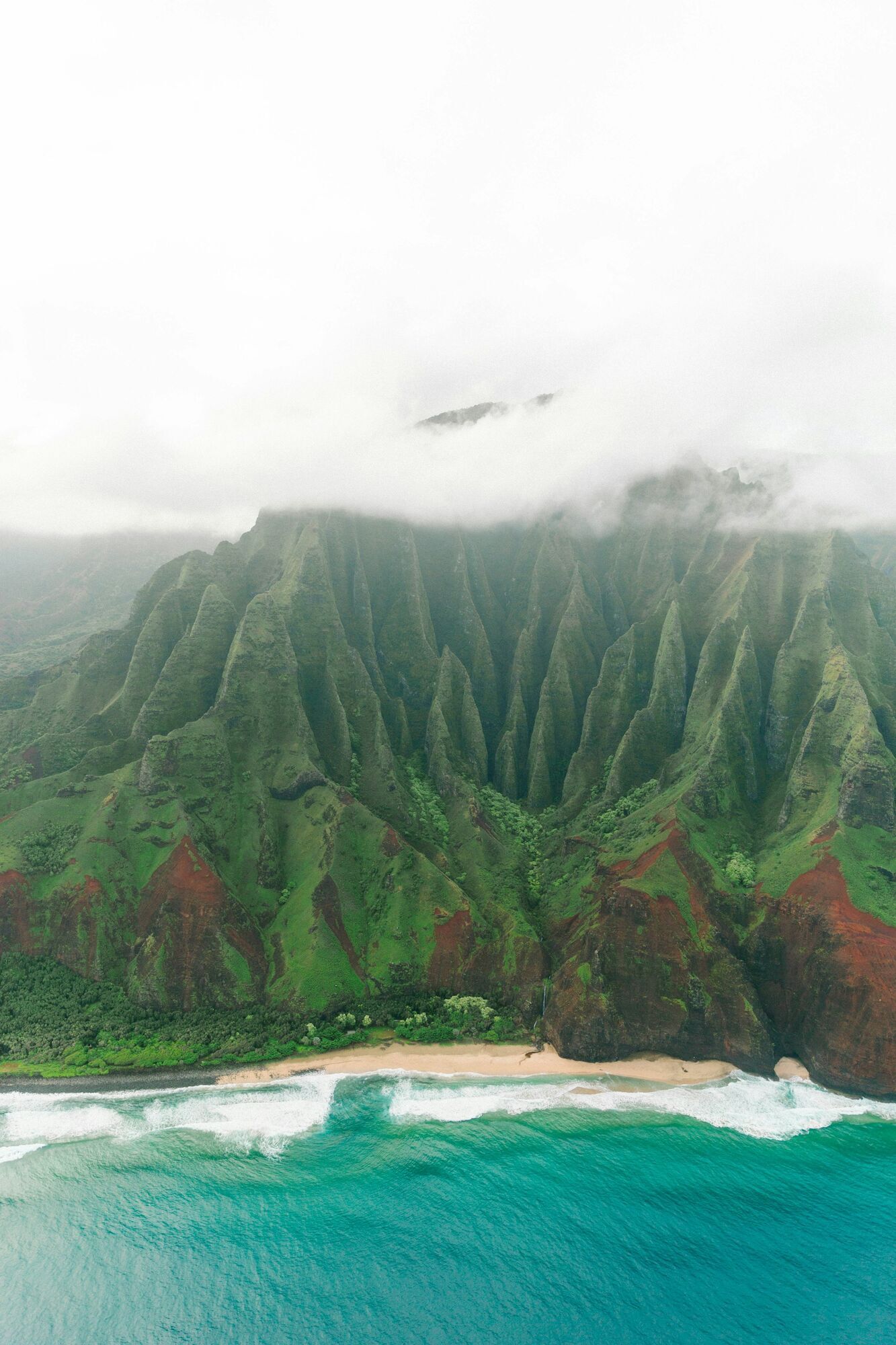 Aerial view of steep green Na Pali Coast cliffs and beach in Kauai