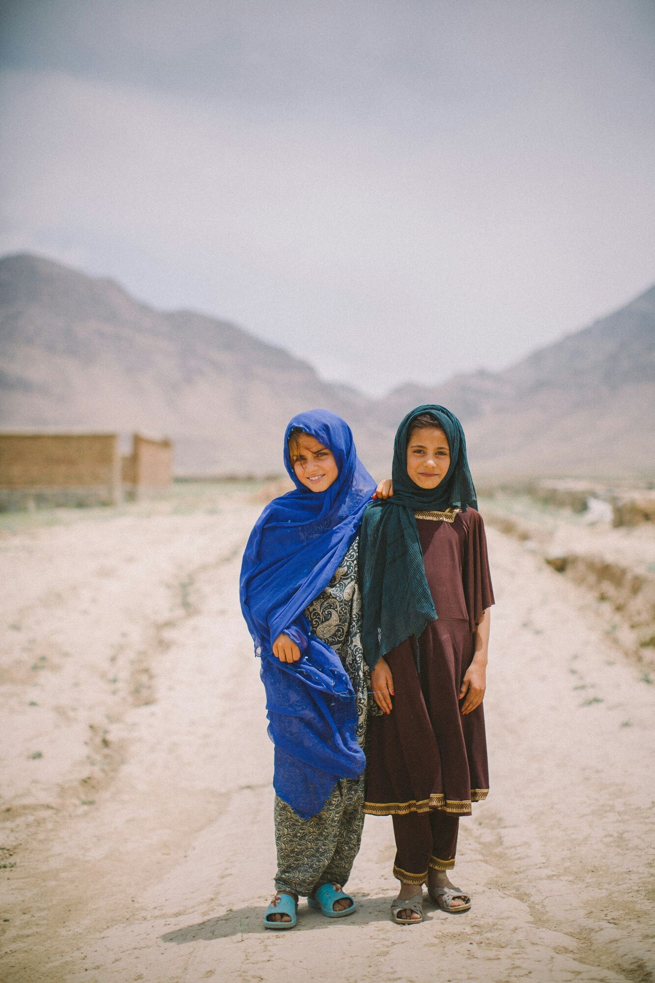 Two girls standing on a rural road with mountains in the background