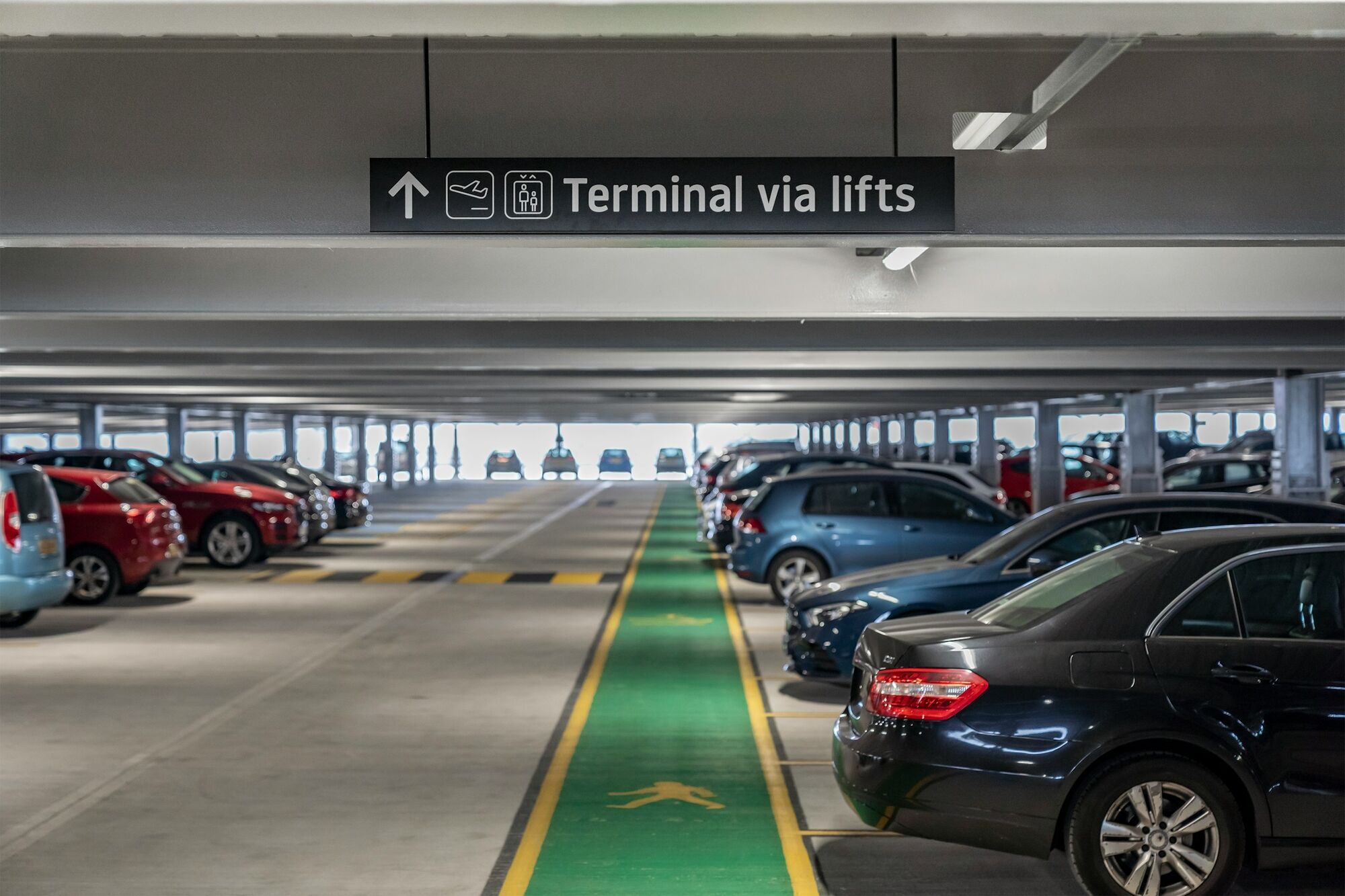 Airport parking garage with sign showing terminal access via lifts