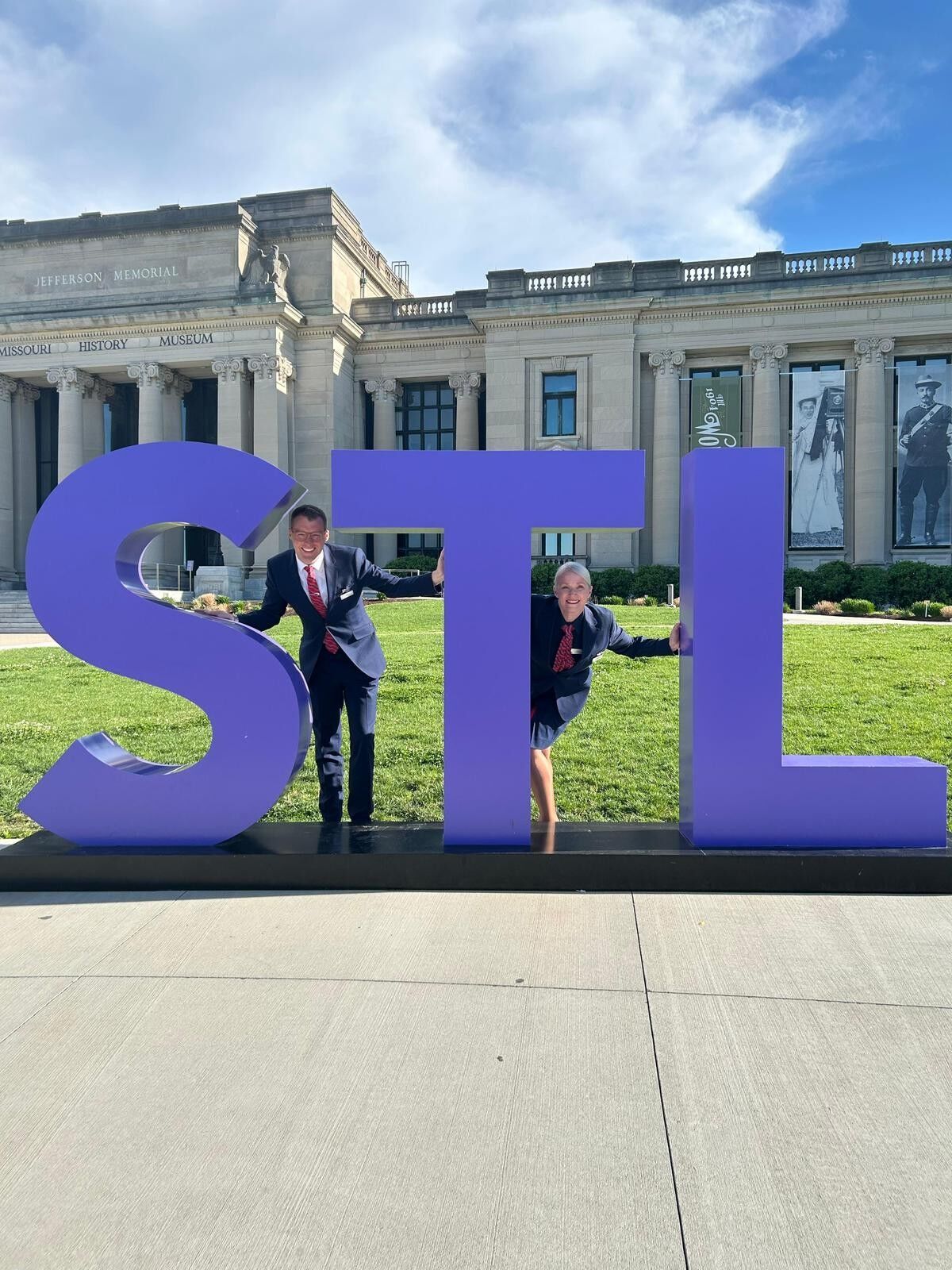 The BA team is standing by large STL letters outside museum in St Louis