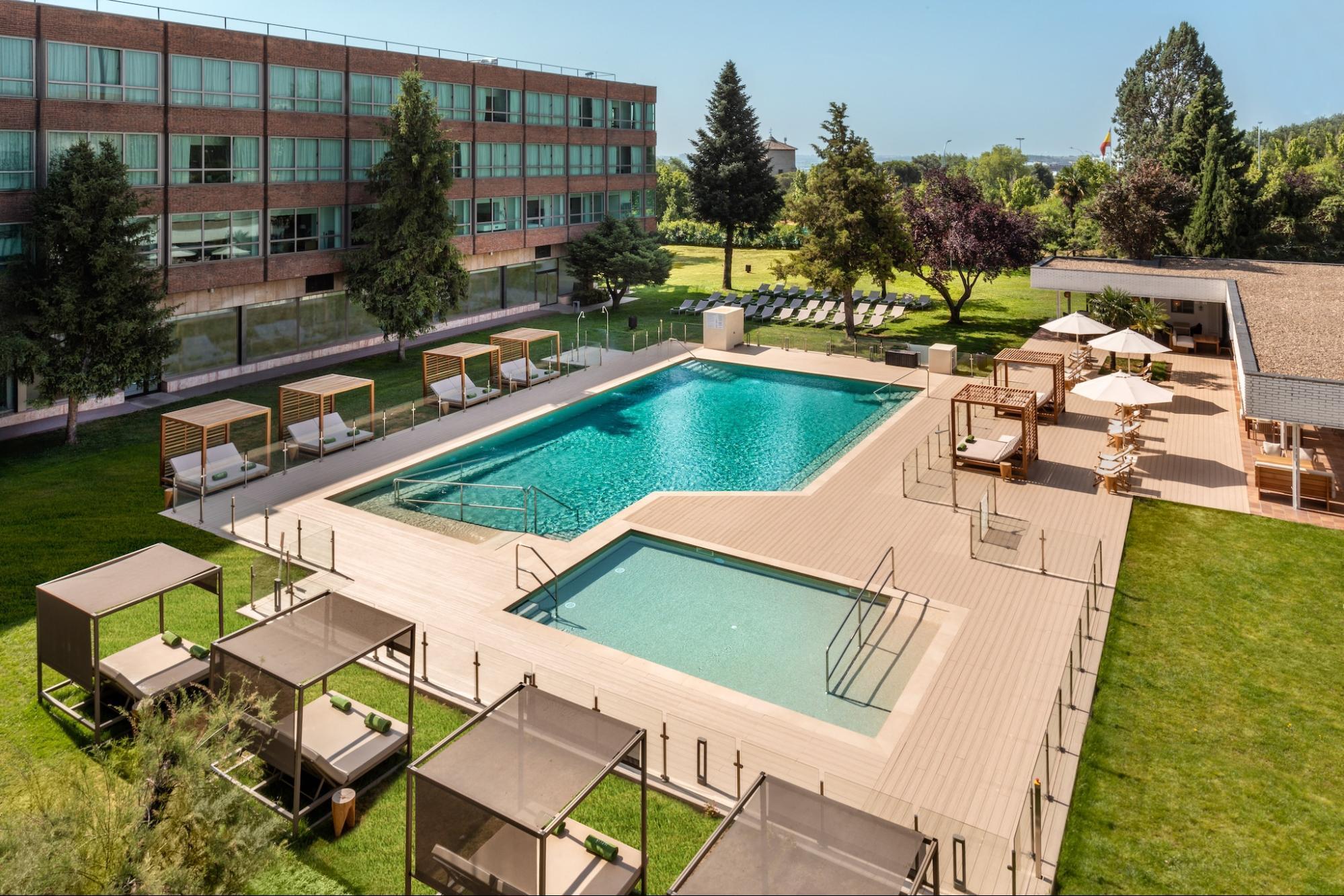 Outdoor swimming pool with sunbeds and garden at Madrid hotel