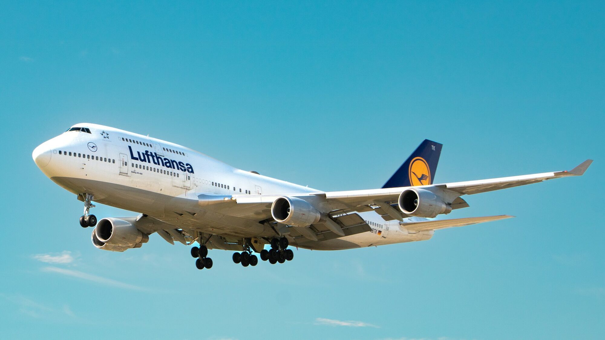 Lufthansa aircraft in flight against clear blue sky with landing gear extended