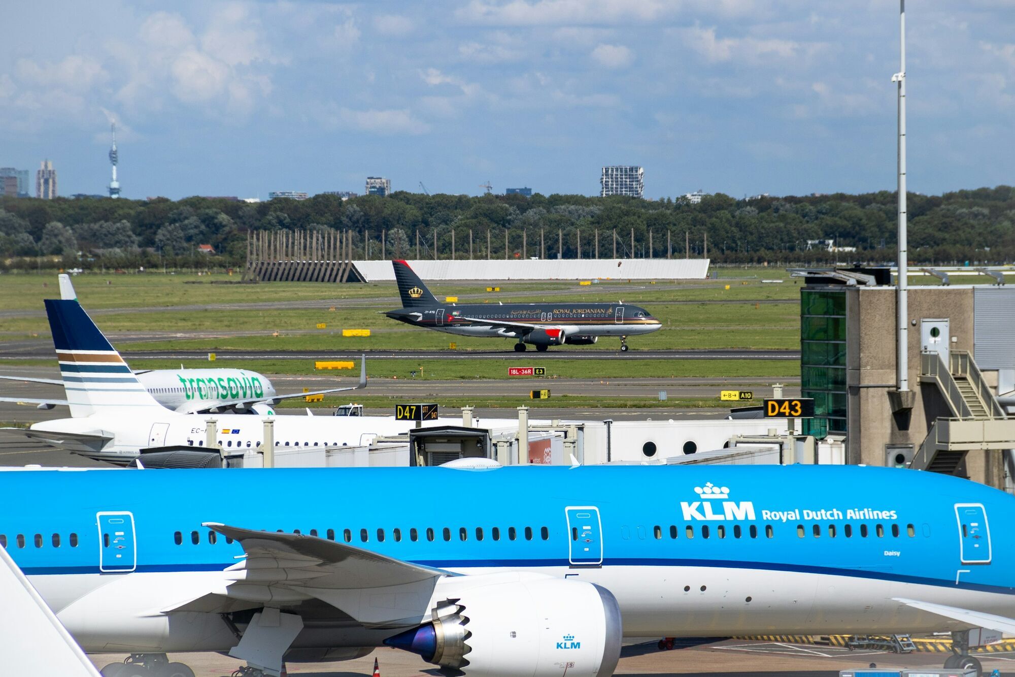 KLM aircraft parked at Schiphol airport with runway traffic in the background