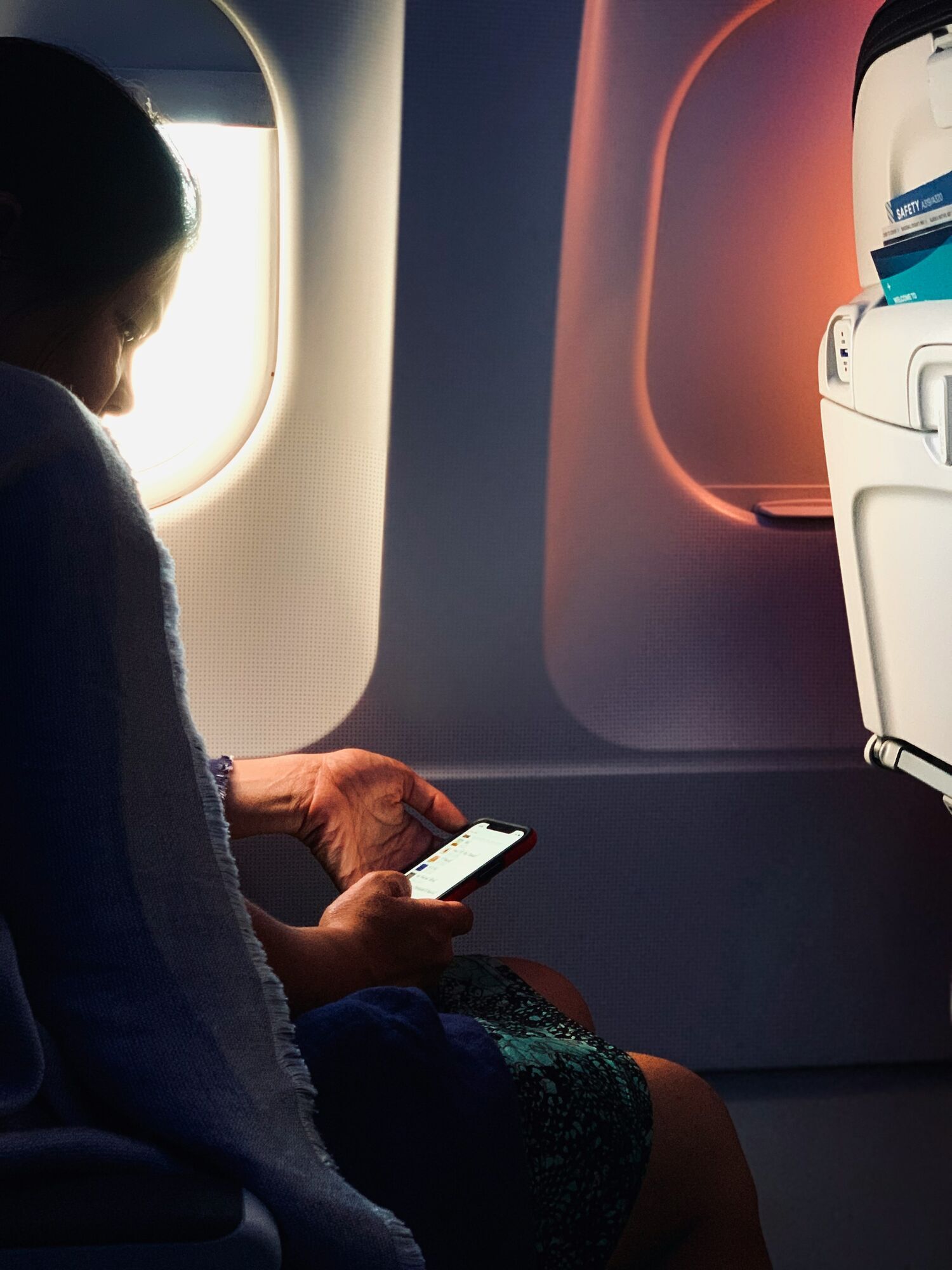 Passenger seated by aircraft window using smartphone during flight
