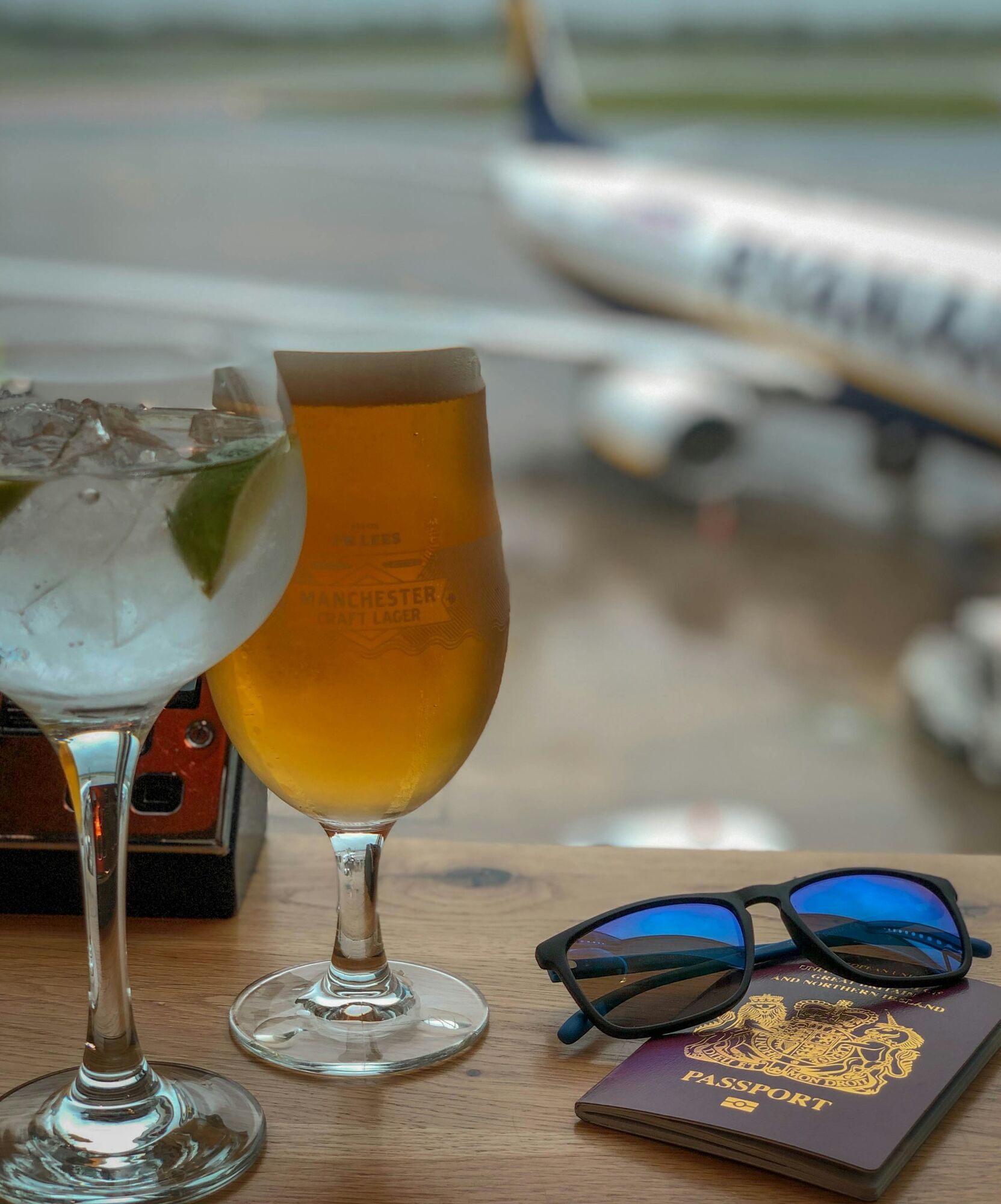 Beer and cocktail on table overlooking airport runway with aircraft in background