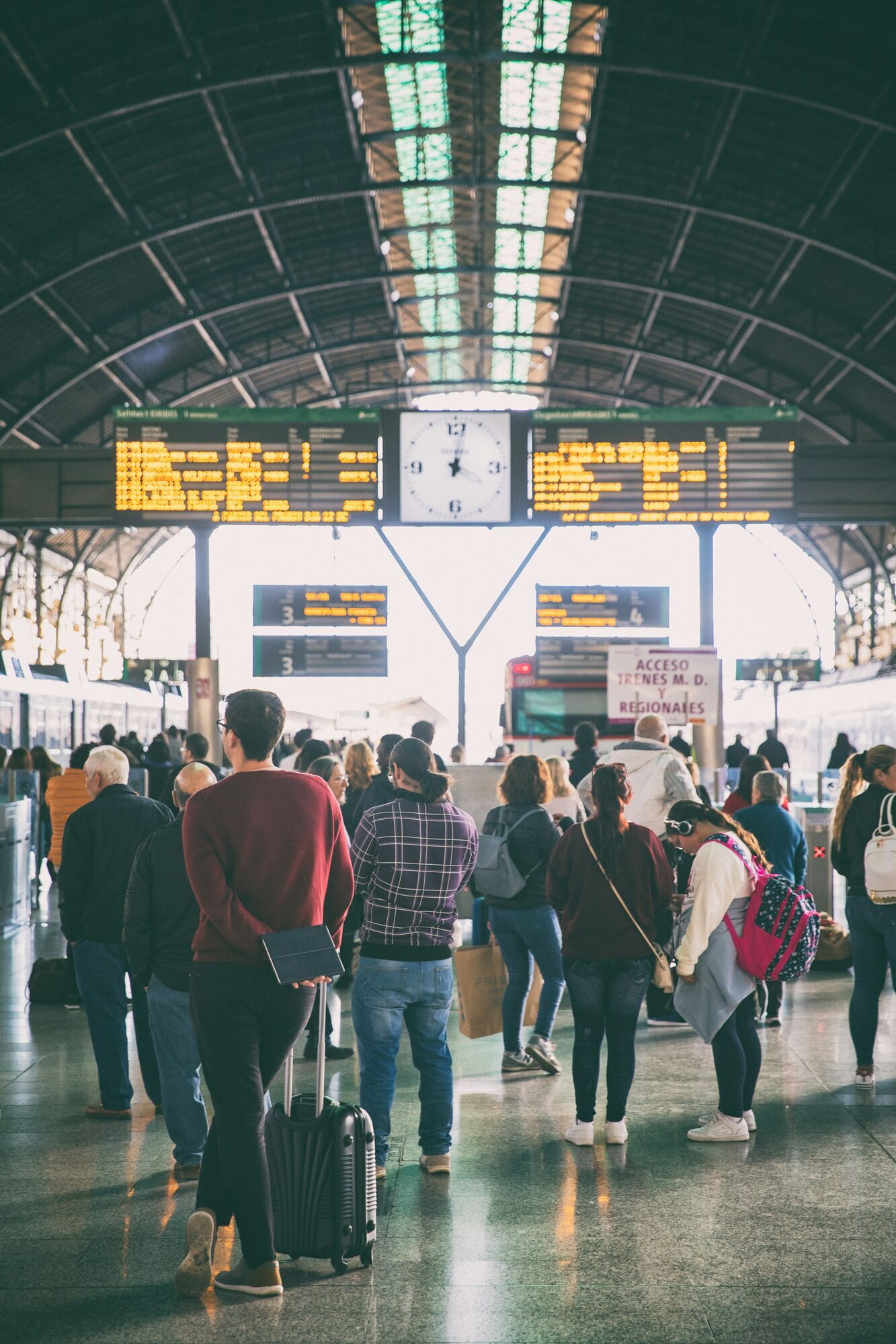 Travellers waiting below departure boards inside a busy terminal
