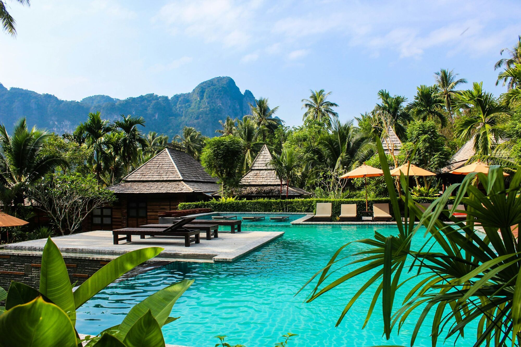 Tropical resort pool surrounded by palm trees and mountains in Thailand