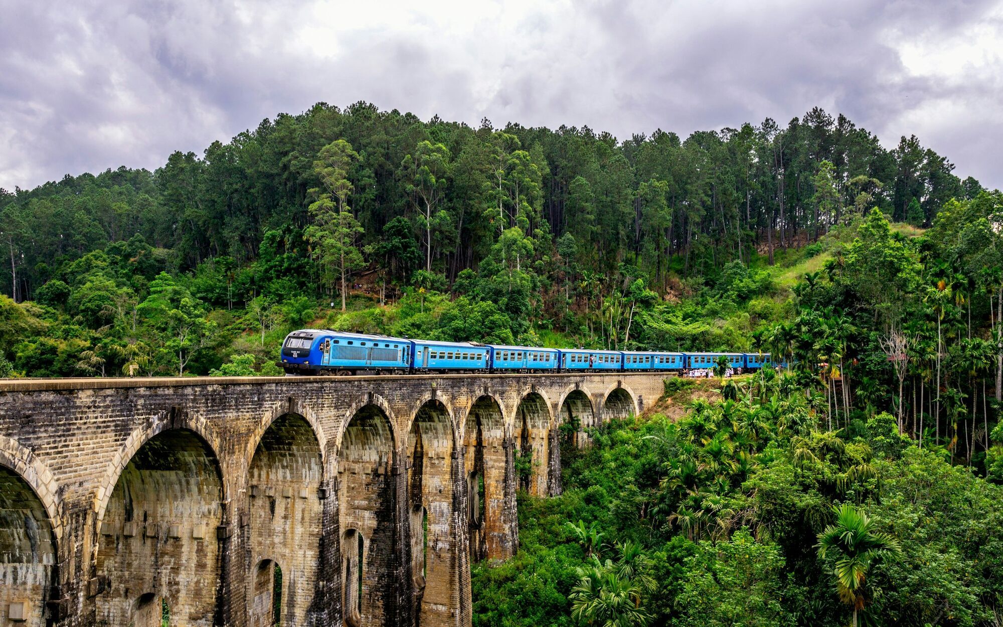 Blue train crossing a stone bridge in Sri Lanka’s green hills