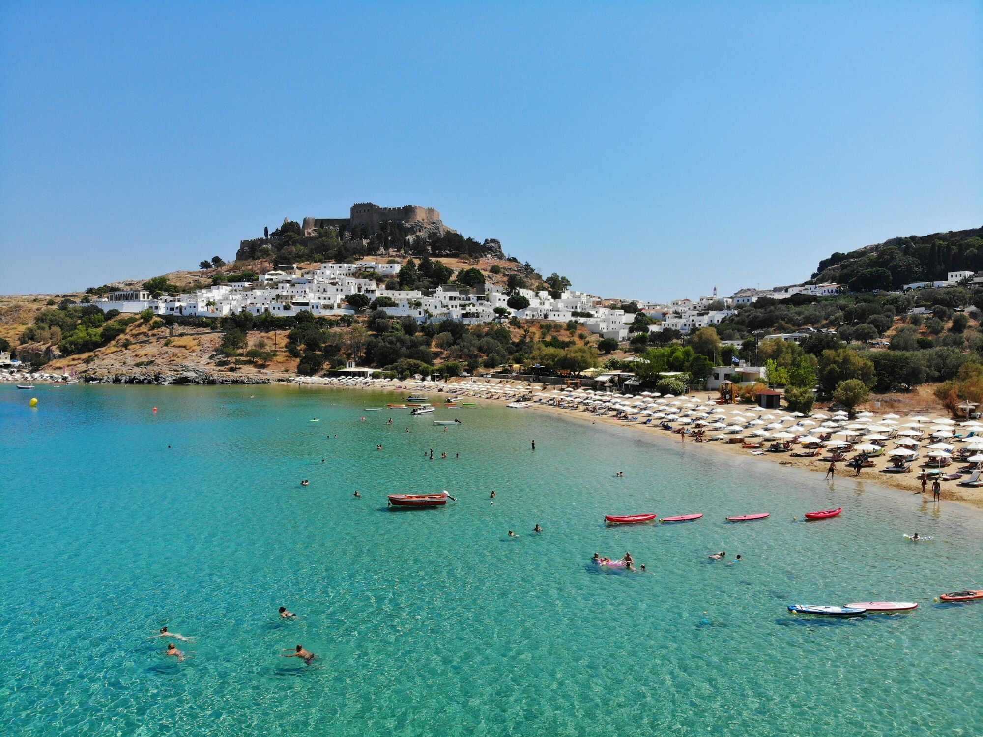 Rhodes beach with clear water, boats and white hillside houses