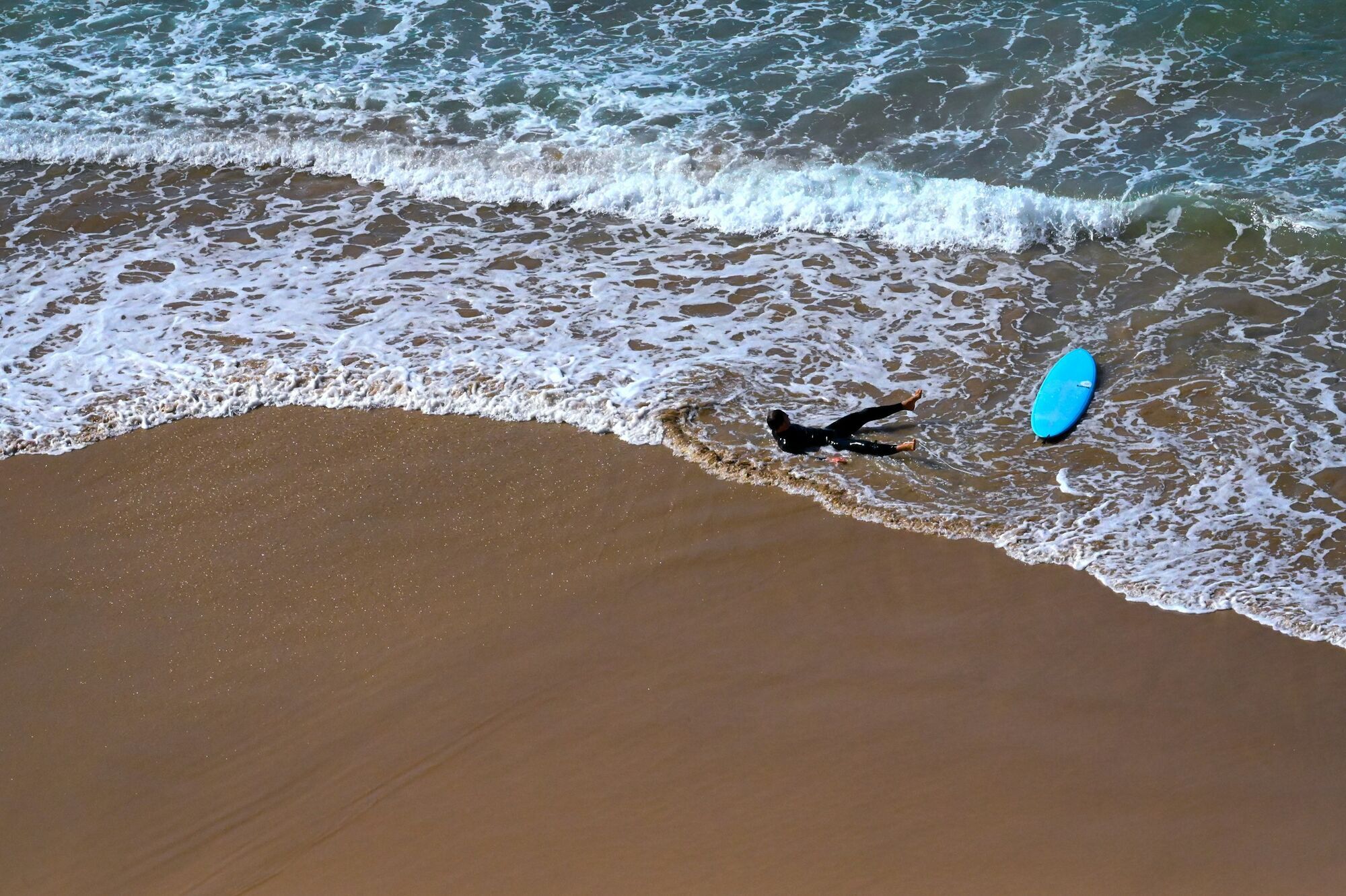 Surfer lying beside a blue board on a sandy beach