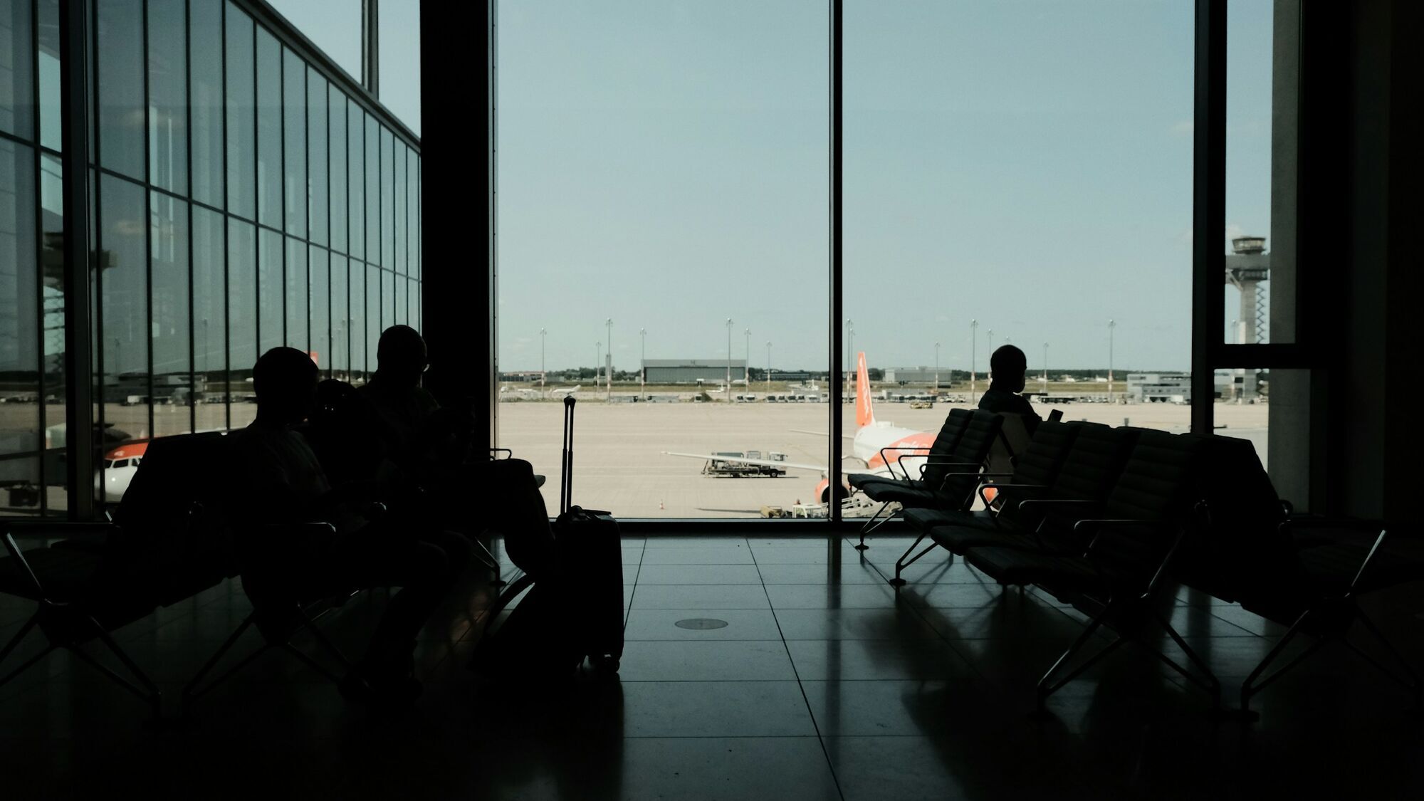 Passengers sitting in airport terminal overlooking runway