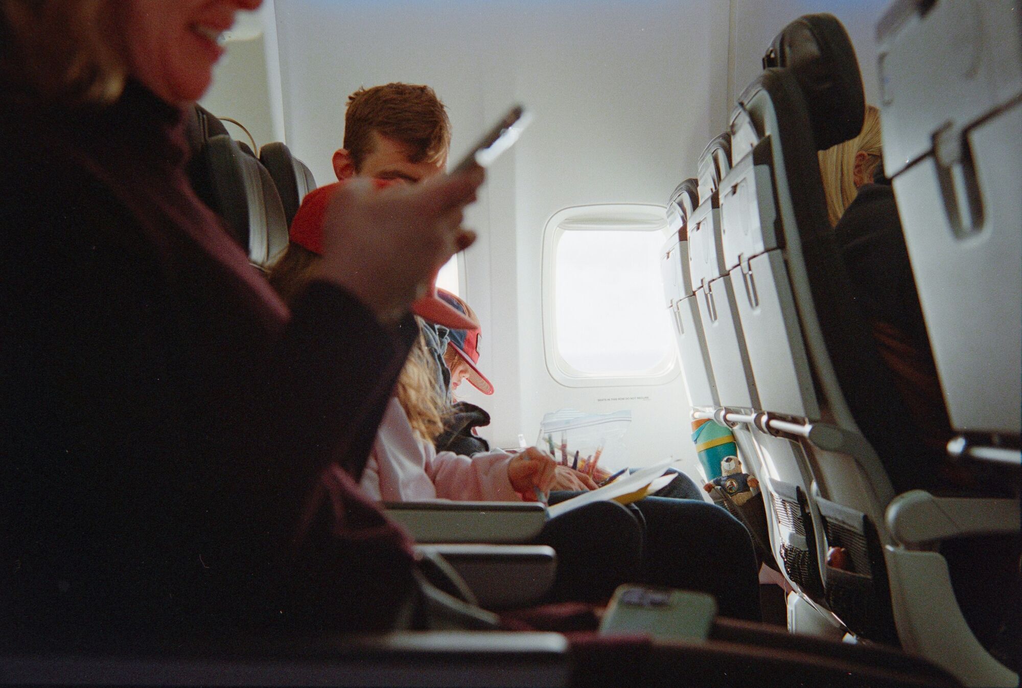 Passengers use devices during a flight while a child draws in an aircraft cabin