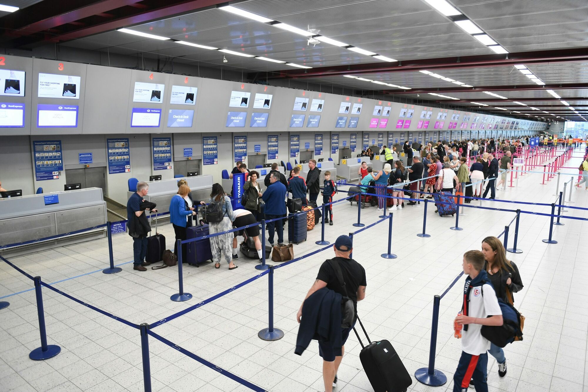 Passengers waiting in airport check-in queues with luggage