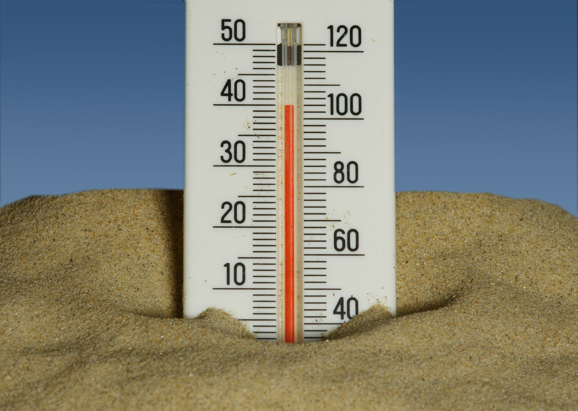 Thermometer showing high temperatures in sand under a blue sky