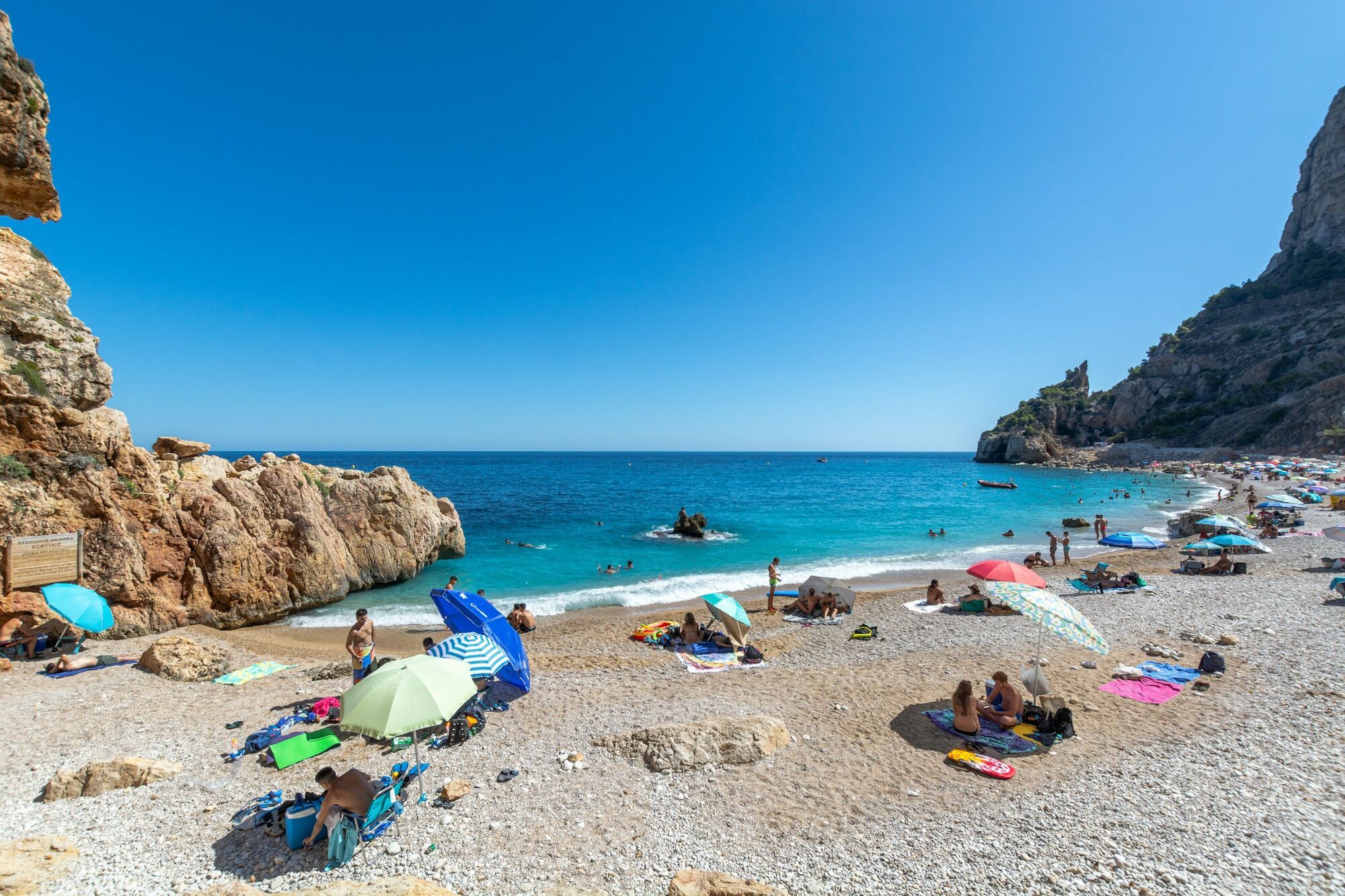Busy Spanish beach with umbrellas and rocky coastline