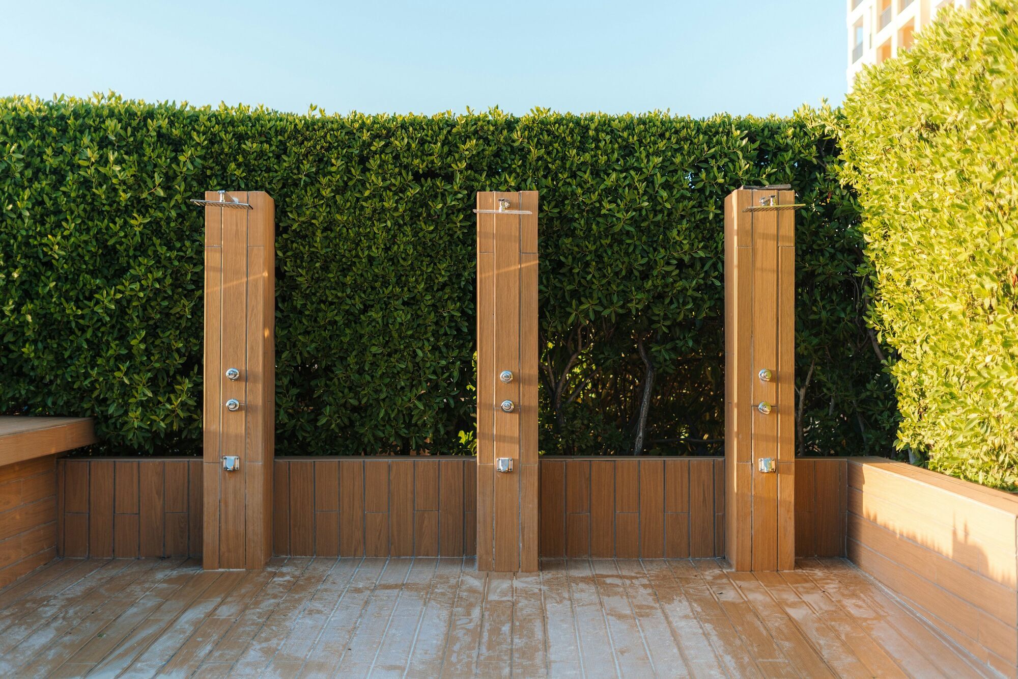 Outdoor beach showers beside green hedges