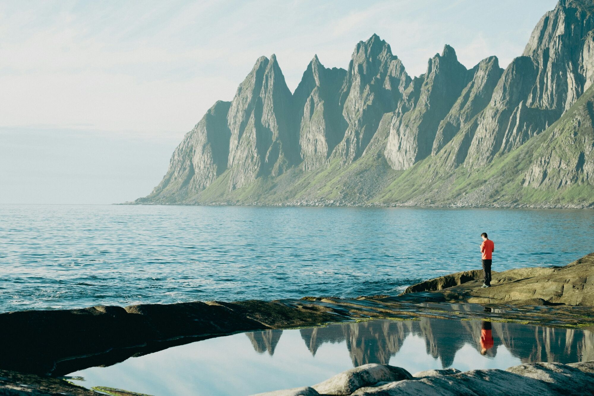 Person standing by Senja’s rocky coast and mountains