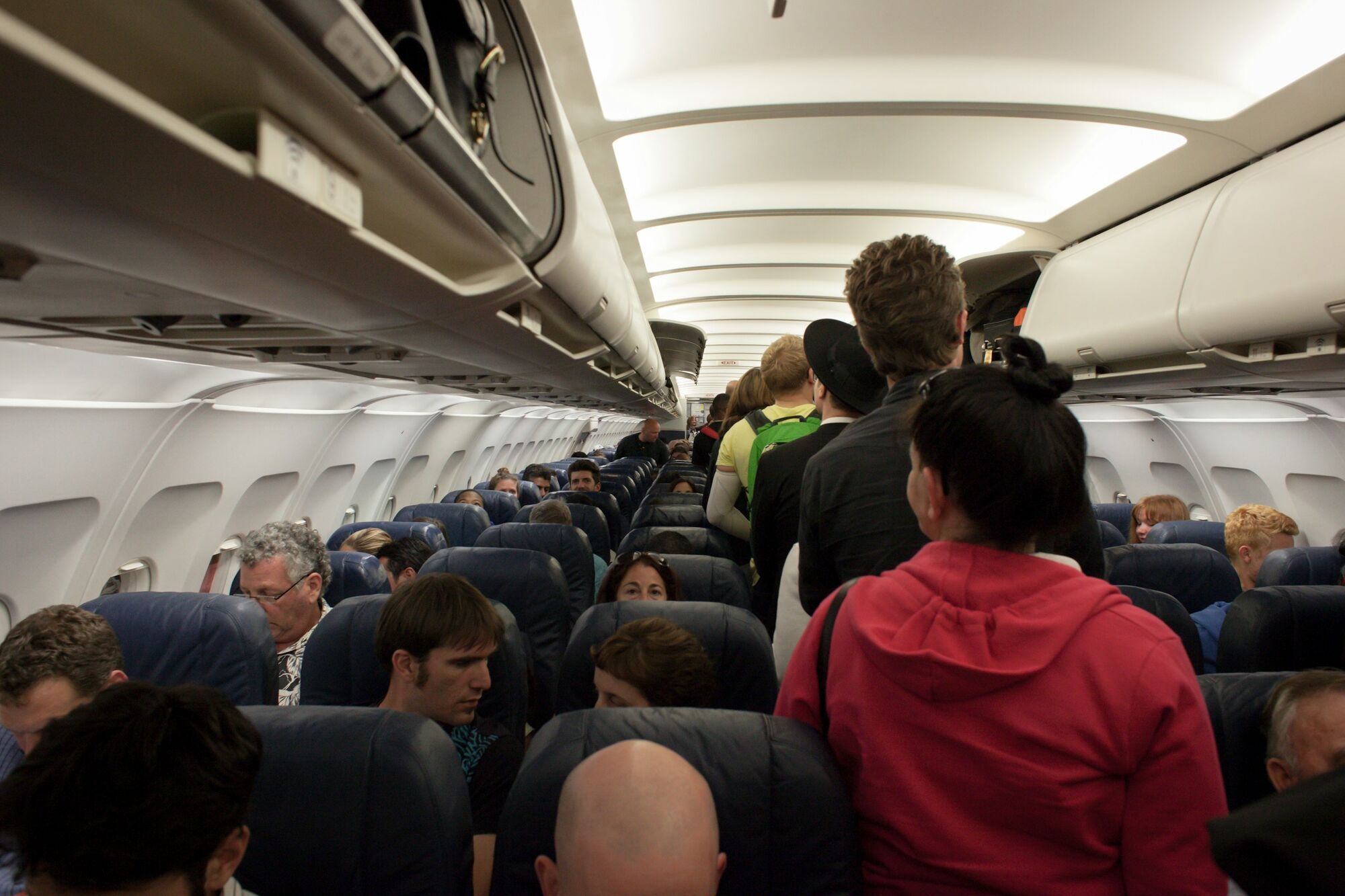 Passengers standing in a crowded aircraft cabin near overhead lockers