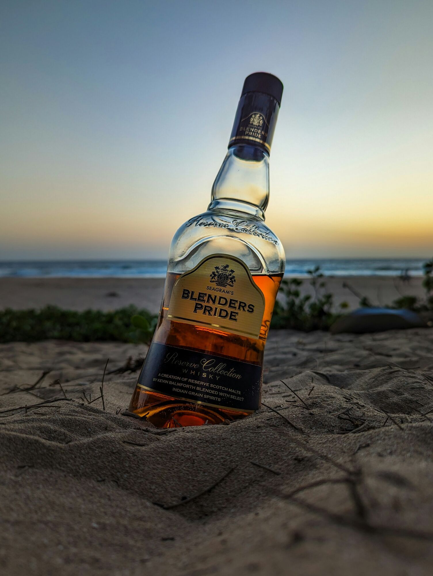 Bottle of alcohol standing on beach sand