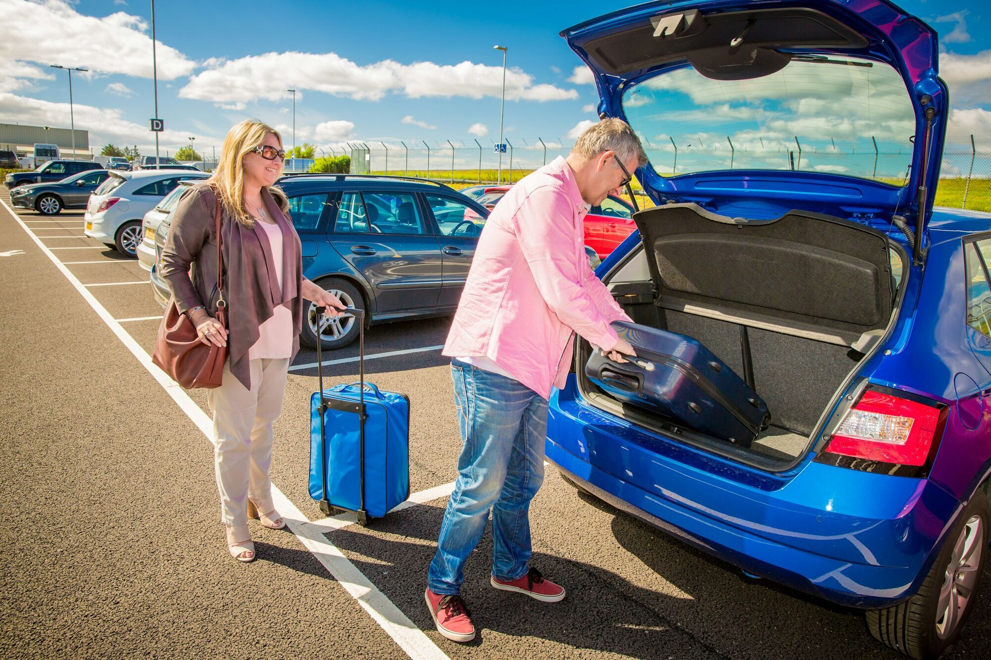 Travellers unloading suitcases from a car at an airport car park
