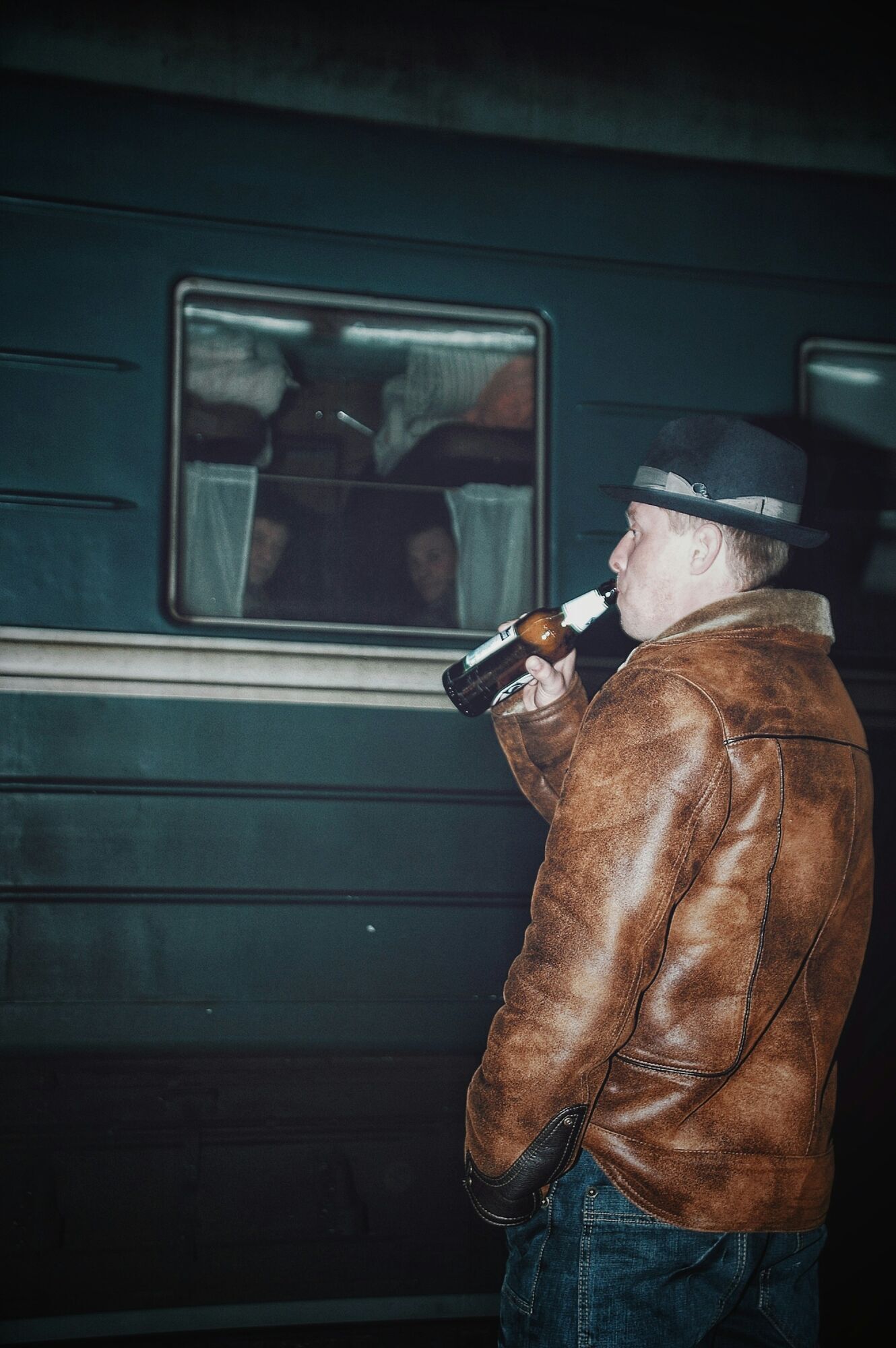 Man drinks beer beside a stationary passenger train