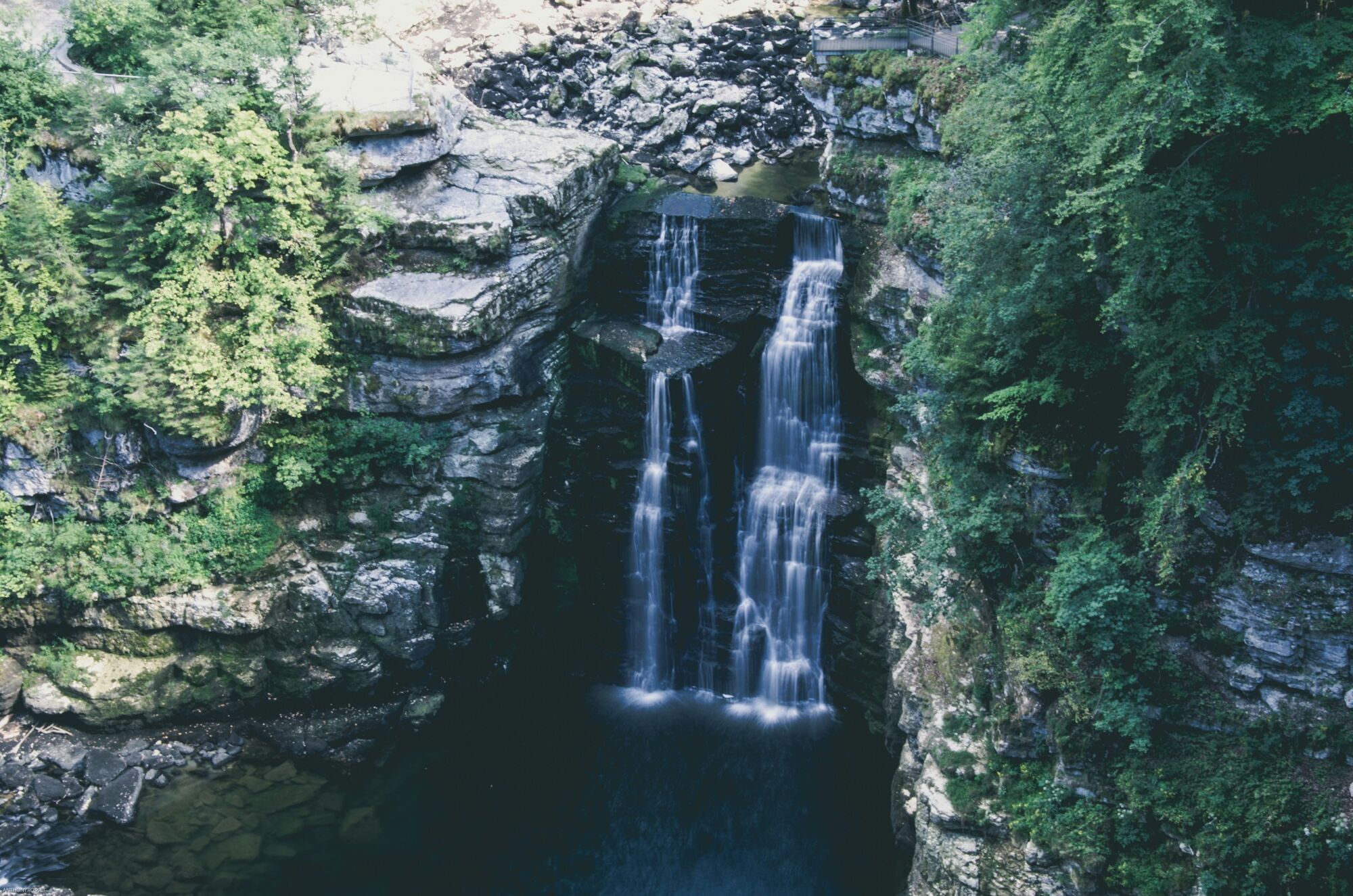 Waterfall cascading through a wooded gorge