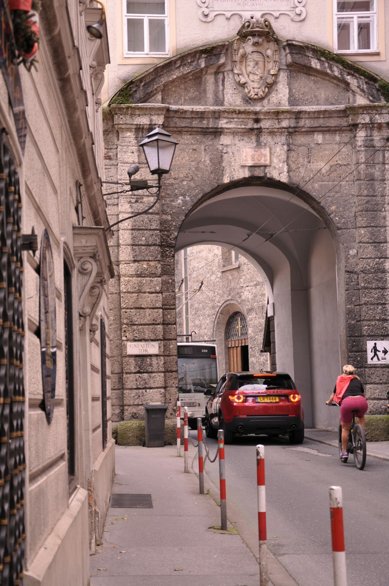 Car and cyclist passing through Salzburg old town gate