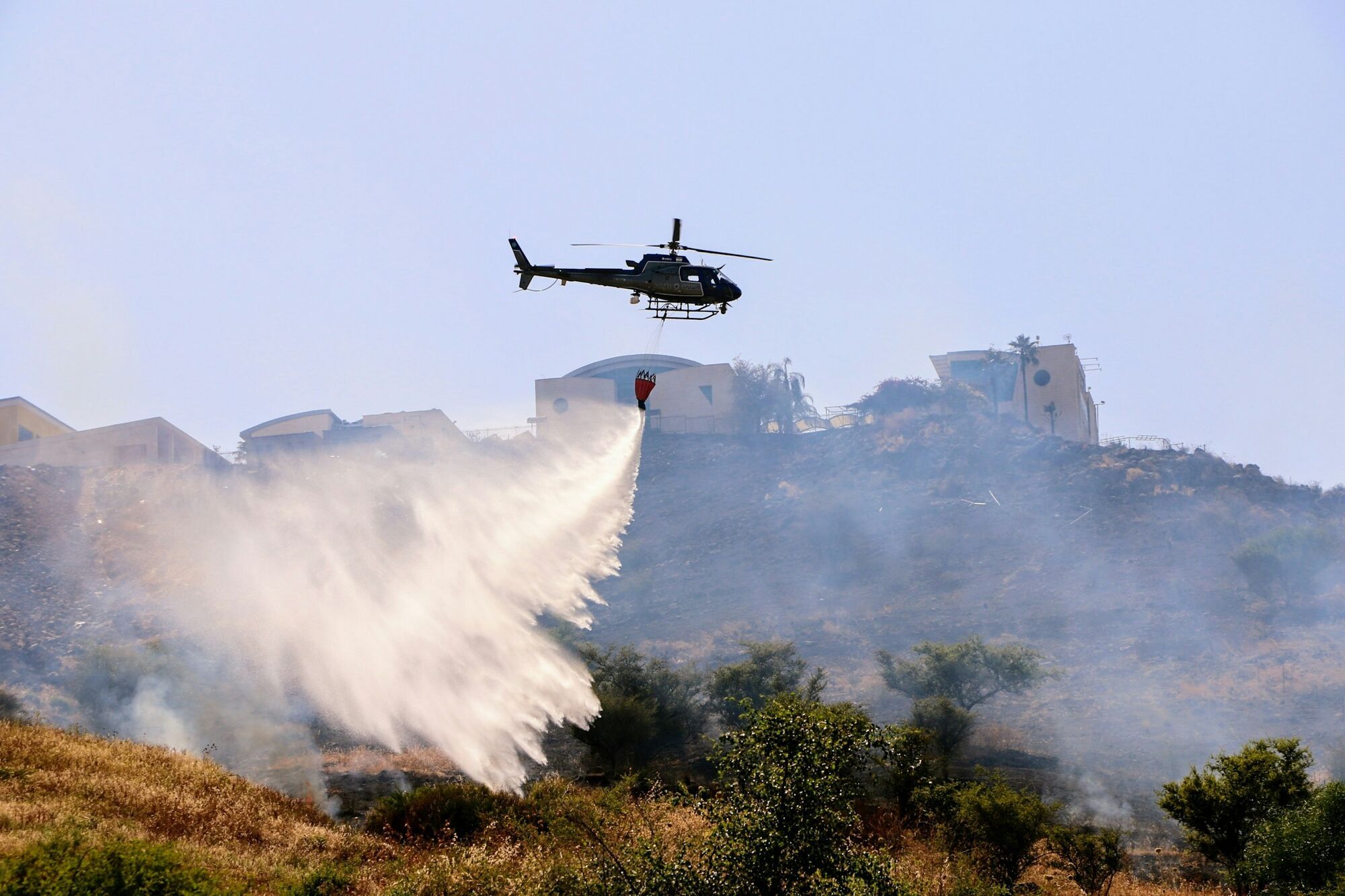 Firefighting helicopter dropping water on a hillside