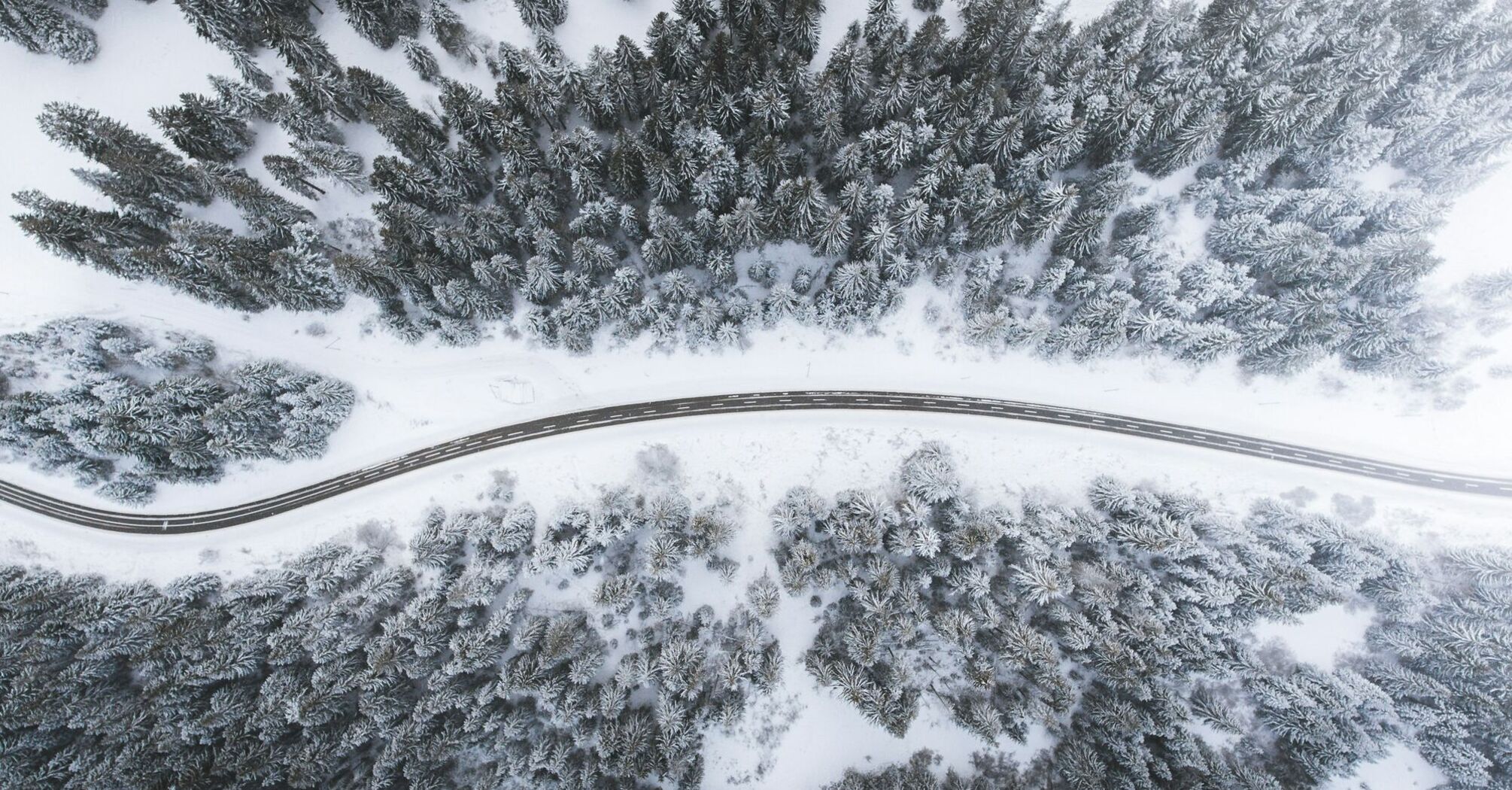 Aerial view of a winding road cutting through a dense snow-covered forest