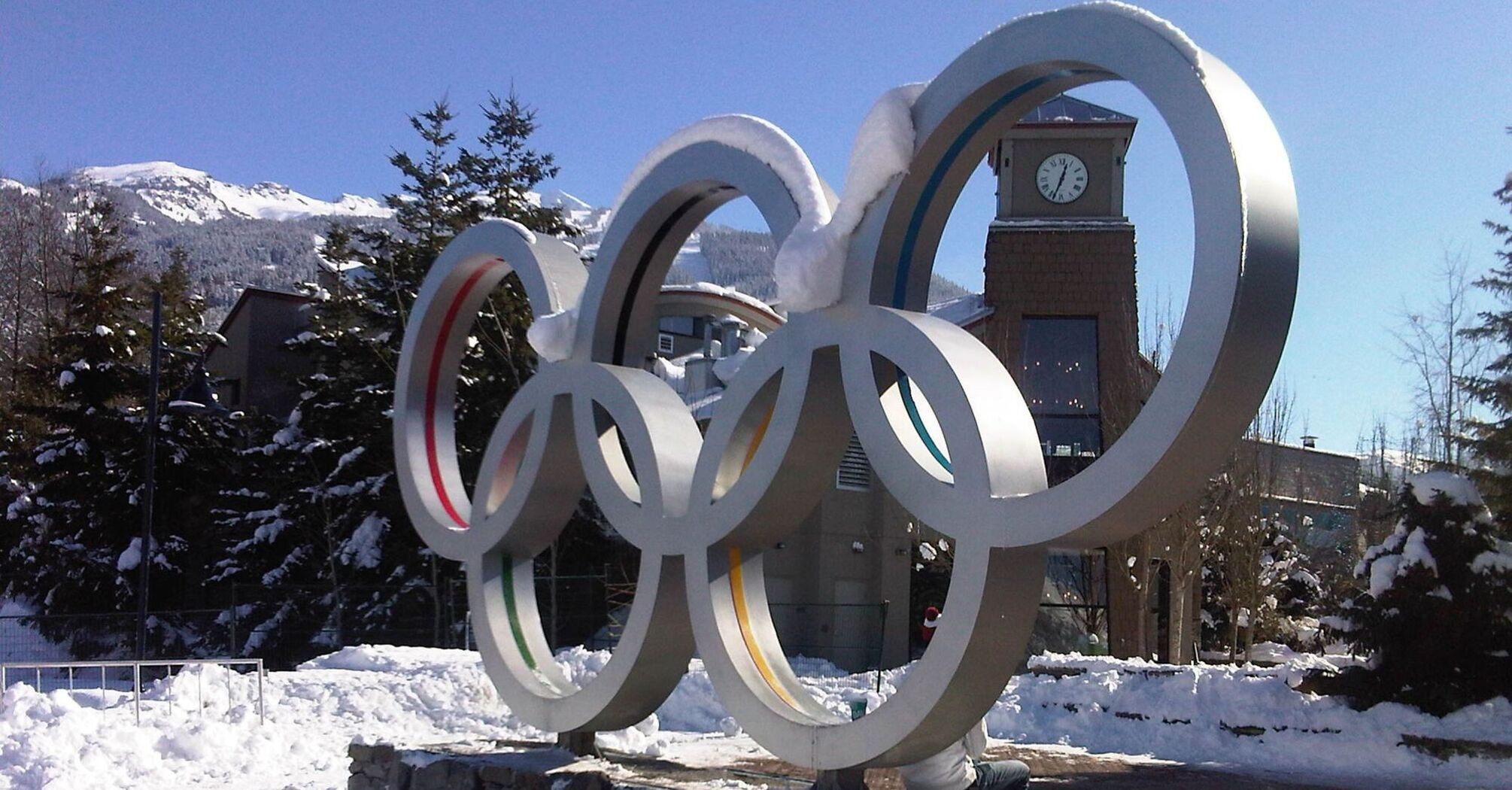 Olympic rings monument on a sunny snowy square with trees in the background