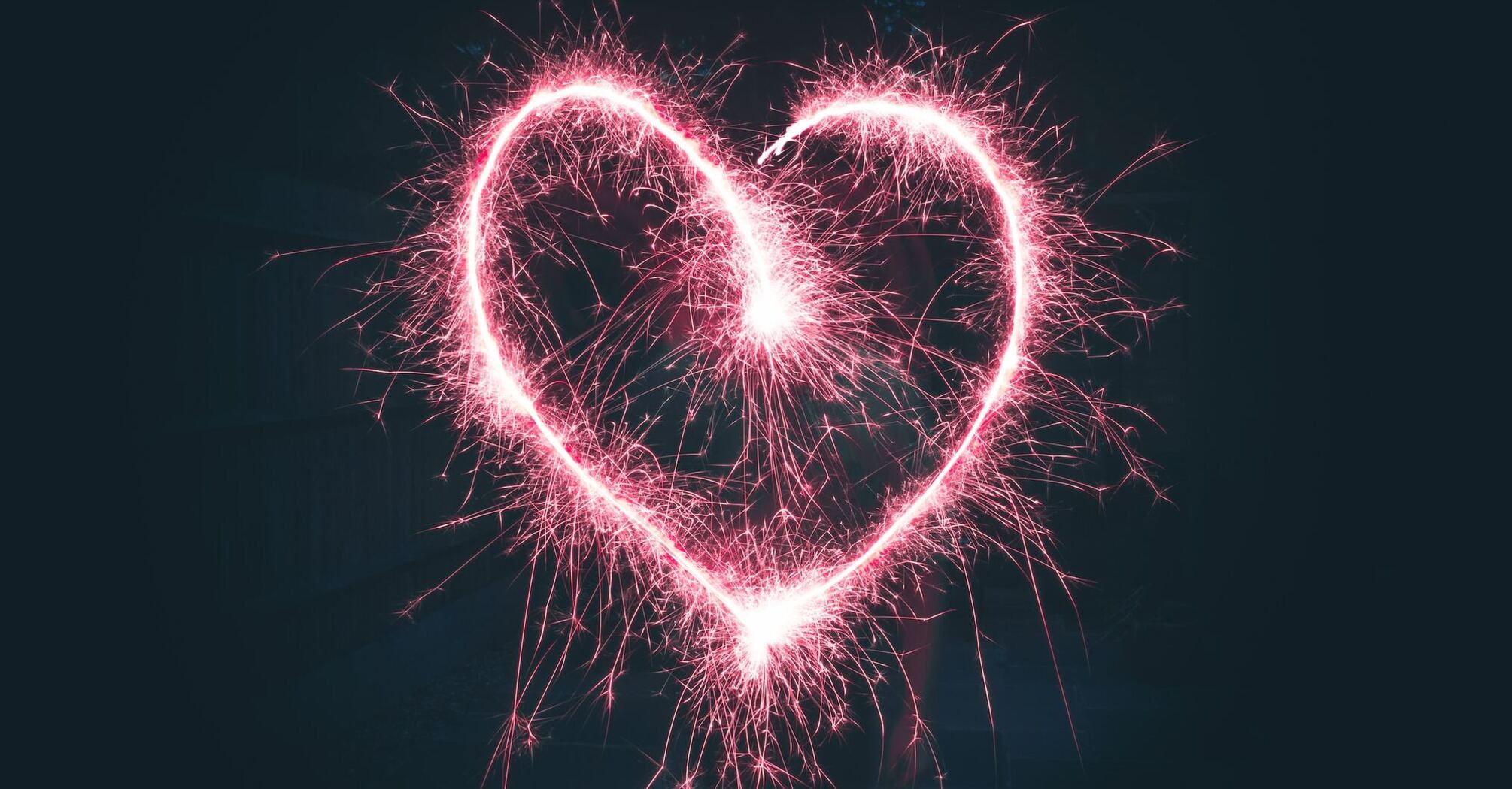 A heart shape created in Valentine's Day with pink sparklers against a dark background 
