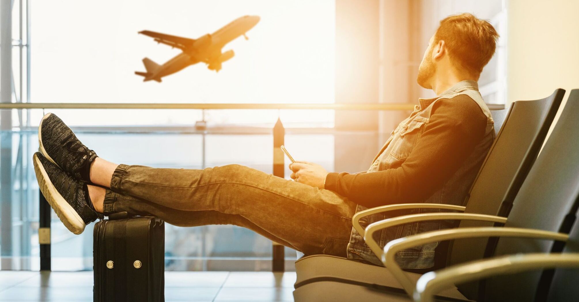 Man sitting on gang chair with feet on luggage looking at airplane