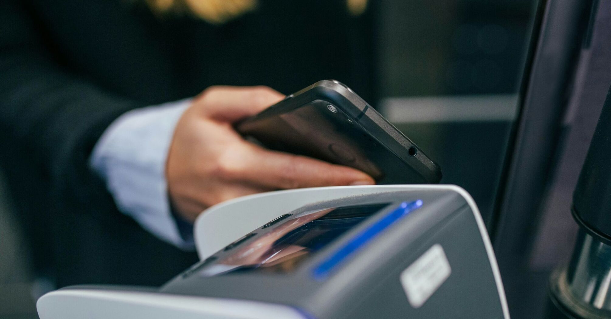 A person shirt is holding a smartphone over a contactless payment terminal