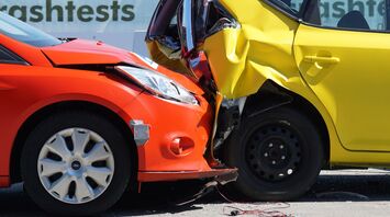 Two cars, one red and one yellow, involved in a collision, depicting a typical road accident that could occur during a road trip