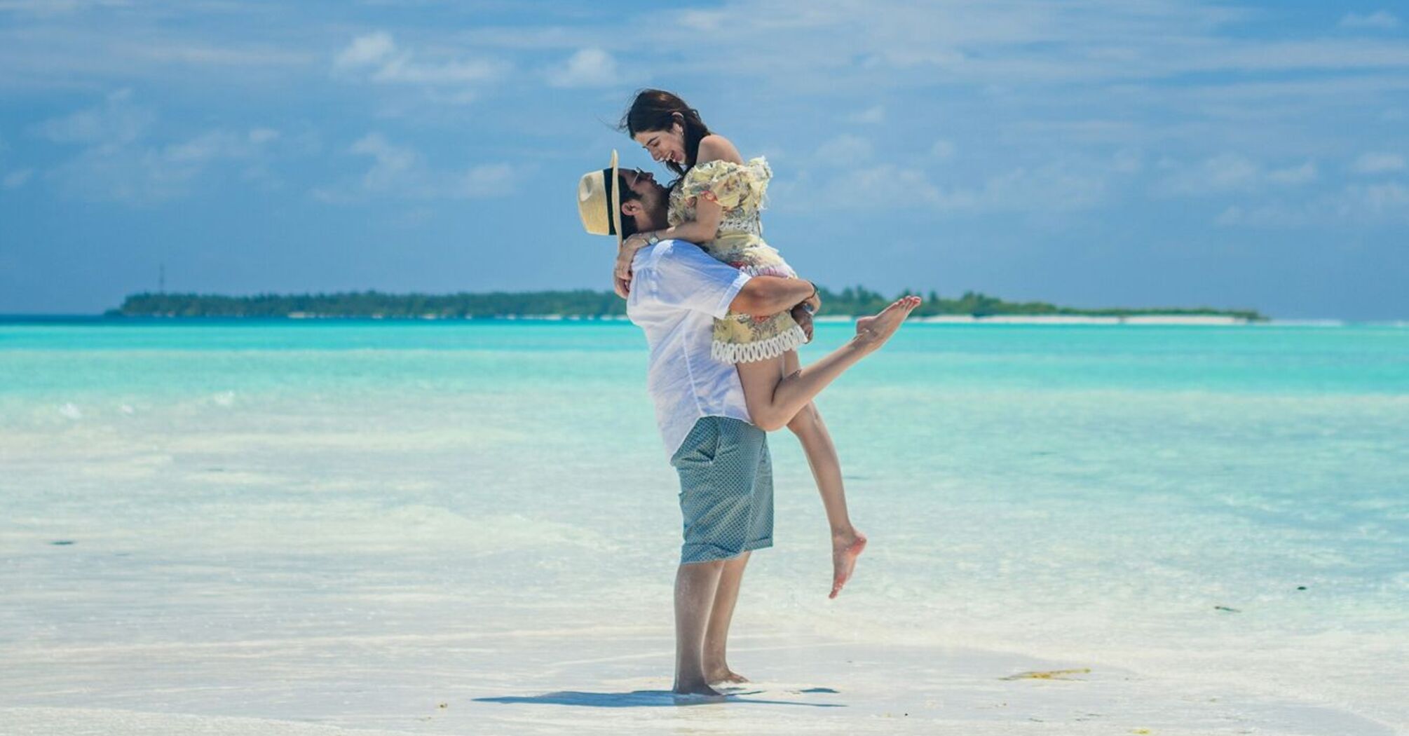 A joyful couple on a tropical beach, with a man carrying a woman in his arms