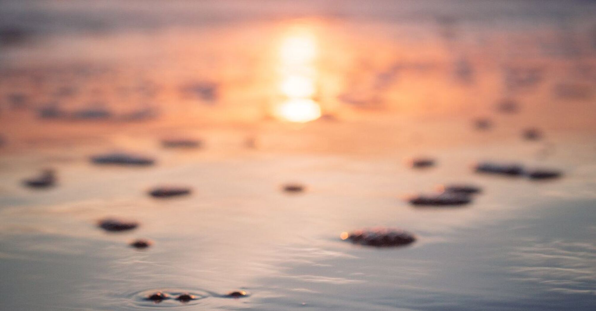 Sunset over a tranquil beach with the sun reflecting on the water and scattered pebbles on the wet sand