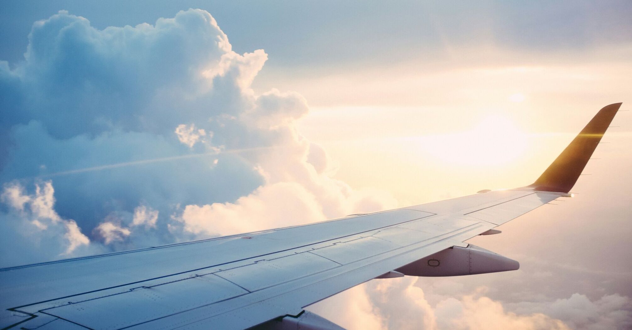 An airplane wing set against the backdrop of clouds and the sun