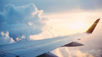 An airplane wing set against the backdrop of clouds and the sun