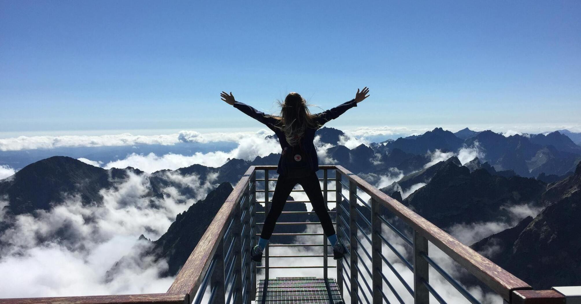Person standing with arms wide open on a mountain viewpoint above the clouds