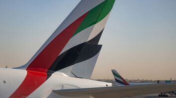 The tail fins of Emirates aircraft showing the distinctive red, green, black, and white design, parked at an airport