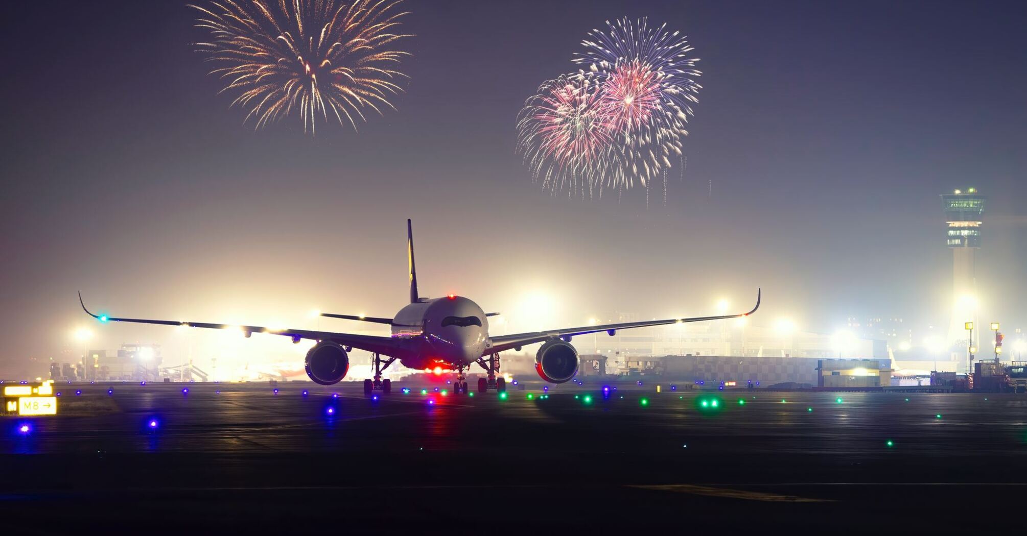 A commercial airplane on a runway at dusk with fireworks in the background