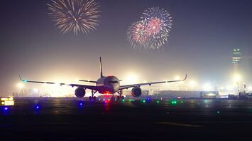 A commercial airplane on a runway at dusk with fireworks in the background