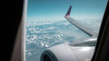 View from an airplane window showing a wing and engine with snow-capped mountains in the background