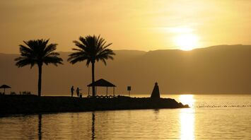 Silhouettes of palm trees and a gazebo against a sunset over the tranquil waters of the Gulf of Aqaba