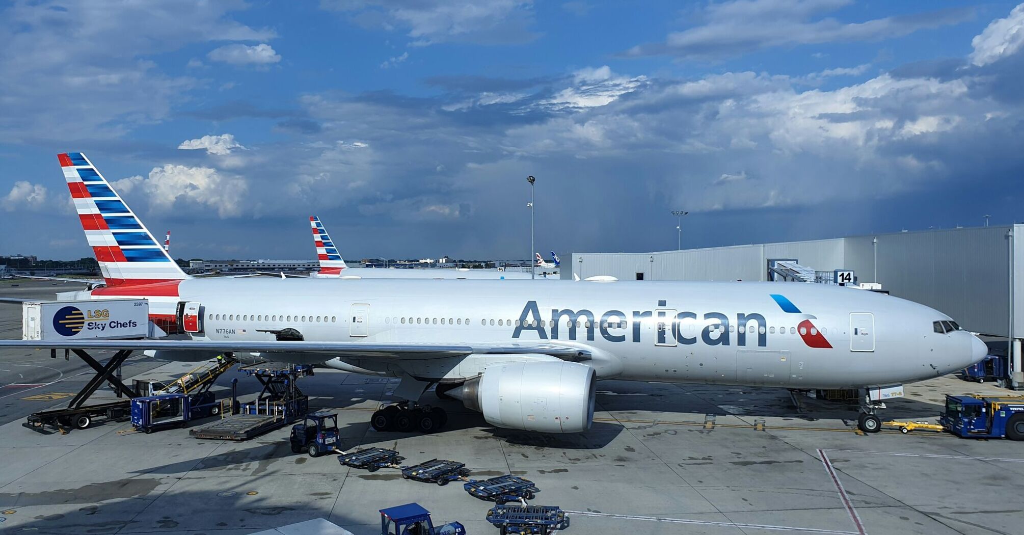 American Airlines aircraft at the airport gate during daytime with service vehicles around and clouds in the sky