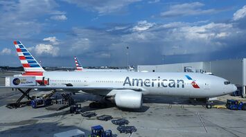 American Airlines aircraft at the airport gate during daytime with service vehicles around and clouds in the sky