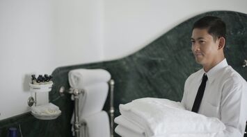 A hotel staff member in uniform is holding fresh towels in the bathroom