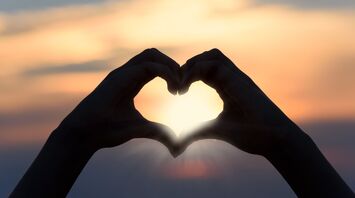 Silhouette of hands forming a heart shape against a sunset sky