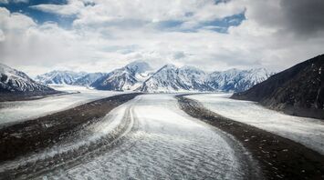 A view of a road winding through snow-capped mountain peaks under a cloudy sky in Yukon