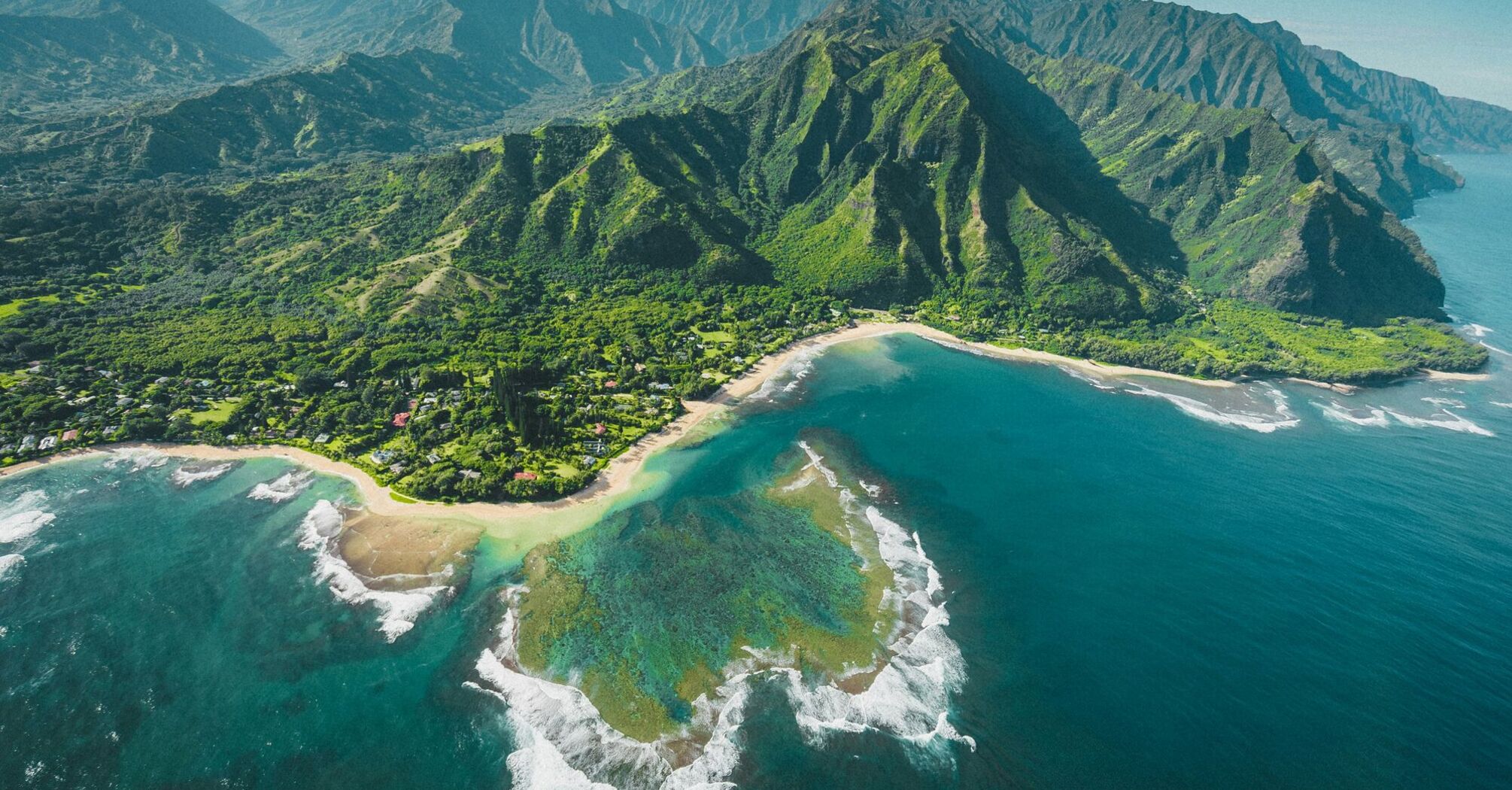 Aerial view of a lush Hawaiian coastline with mountains, beach, and clear blue waters
